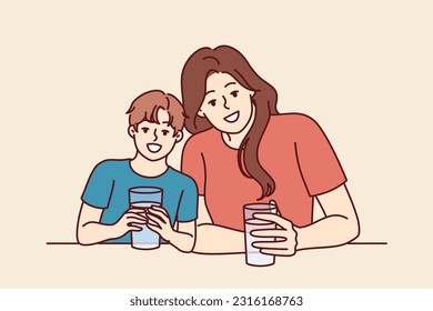 Feliz madre e hijo beben agua de gafas transparentes y sonríen disfrutando de refrescantes bebidas. Familia positiva con agua mira la cámara juntos y sonríe urgiendo a beber más líquido