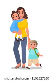 Happy mommy is walking with her little son and daughter. The baby girl is sitting on the mothers hands and holding her by the neck. The boy is walking with mom by the hand and carrying a backpack.