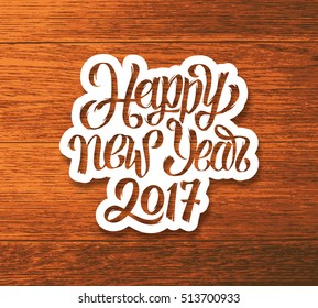 Happy New Year 2017 greeting card design. Sticker with hand lettering inscription on wood background. Vector festive ilustration with typography.