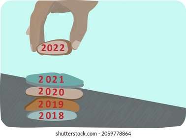 Happy new year 2022 is coming, hand adding stone to pebble tower because new year 2022 replace 2021. Beautiful conceptual photo with text for holiday and greeting cards.