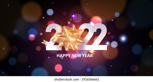 Happy new year 2022. Golden self adhesive gift bow with white numbers on defocused colorful, bokeh background. Holiday greeting card design.