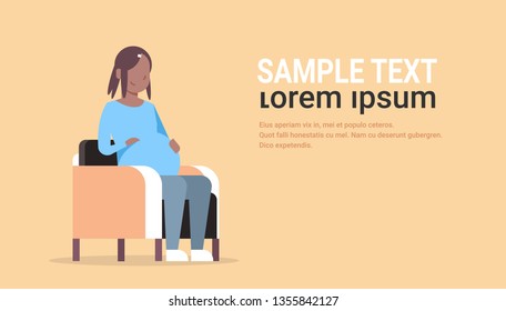 happy pregnant african american woman sitting in armchair girl holding her bump pregnancy and motherhood concept flat full length horizontal copy space