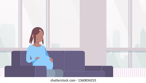 happy pregnant african american woman sitting on couch girl holding her bump pregnancy and motherhood concept modern home living room interior flat portrait horizontal
