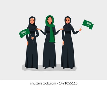 Happy Saudi women celebrate the Independence Day of the Kingdom of Saudi Arabia. Muslim girls dressed in black Abaya hold the KSA flags on the national day-September 23.