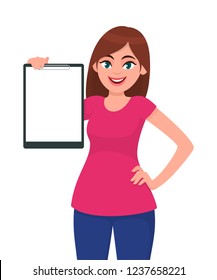 Happy smiling beautiful young woman 
holding / showing a blank clipboard while holding hand on hip, standing against white background isolated. Concept illustration in vector cartoon flat style.