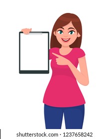 Happy smiling beautiful young woman 
holding / showing a blank clipboard and pointing towards, while standing against white background. Human gesture concept illustration in vector cartoon flat style.