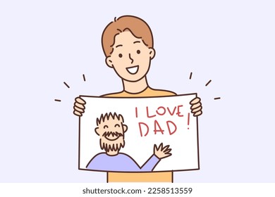 Happy teenager boy holding poster and inscription I love dad   image man in hands  Positive schoolboy demonstrates prepared gift handmade drawing and portrait dad for Father Day