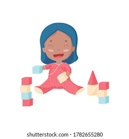 Happy toddler plays bricks and builds castle. Afro American kid in pink pajamas laughing and playing toys/