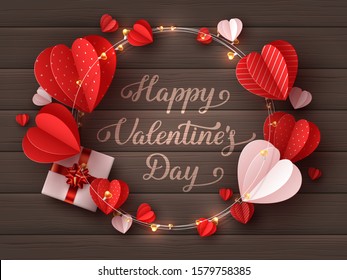 Happy Valentines day greeting card. Decorative paper cut hearts, gift box, garland with handwritten lettering text on brown wooden background. Vector illustration.