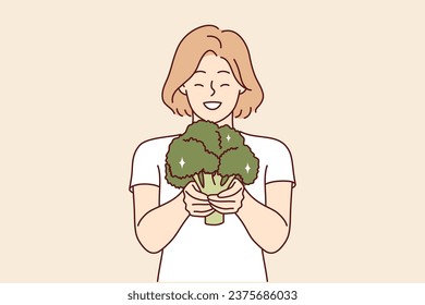 Happy woman with broccoli in hands recommends going vegan and eating only fresh organic vegetables. Smiling girl holding broccoli filled with useful vitamins for body and immunity.