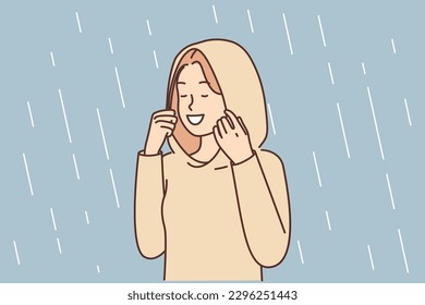 Happy woman enjoys autumn rain standing in autumn raincoat with hood that protects against drops. Positive girl relish spring weather and precipitation with storm rain after long drought