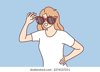 Mujer feliz con gafas de sol gigantes sonrisas en la cara y mira a su alrededor buscando conocidos. Chica positiva con camiseta informal de gafas de sol departamentales por ir a la playa o caminar en el parque de verano 