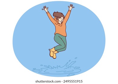 Happy woman jumping in puddle enjoying first autumn rain after hot summer. Girl in good mood in casual clothes jumps standing in puddle, receiving positive emotions from long-awaited walk