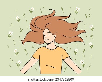 Una mujer feliz con el pelo largo yace sobre el césped en el parque con los ojos cerrados y sonríe regocijándose a la luz del sol. Mujer joven positiva en camiseta informal disfrutando del buen tiempo del verano en el césped con flores