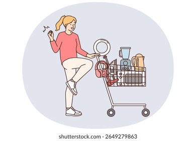 Happy woman with shopping cart and supermarket filled with electronics won in competition. Positive young girl rejoices at bargain purchase of electronics for home in mall or marketplace