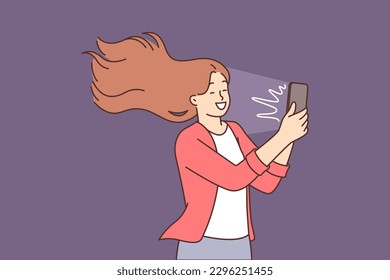 Happy woman takes selfie on mobile phone camera and smiles standing with hair blowing in wind. Positive girl likes to take selfie or chat via video call on smartphone with friends.