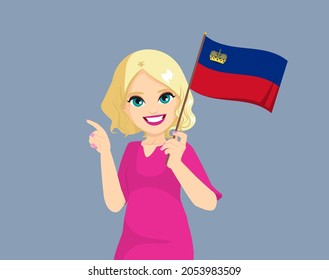 Happy young blonde curly haired white woman holding Liechtenstein flag and making pointing finger gesture