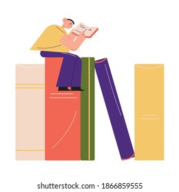 Happy young boy sitting on colorful books and reading story in book in library