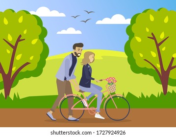 Happy young man is helping a smiling woman to ride a bicycle on the road at summer forest background. Girl is riding a pink bicycle with a bouquet of flowers in a basket. Romantic ride in the park