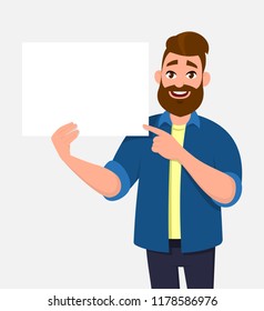 Happy young man holding/showing/displaying white blank board/banner/poster and pointing index finger towards that. Concept illustration in vector cartoon style.