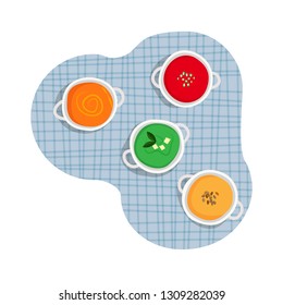 Healthy cuisine set of white ceramic pots of various cream soups - tomato, carrot, broccoli, pumpkin cream soup on blue tartan table cloth background. 