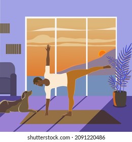 Healthy fit African American man performing Utthita Trikonasana or Triangle Pose indoors on the sunset with a dog