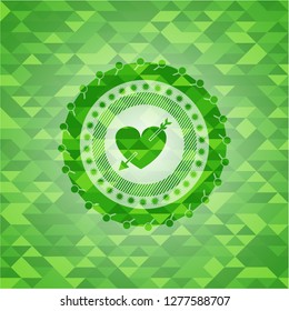 heart with arrow icon inside green emblem. Mosaic background