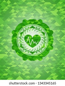 heart with electrocardiogram icon inside green emblem with triangle mosaic background