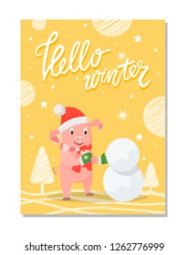 Hello winter poster with pig in red hat and knitted scarf making snowman outdoors. Piglet in warm cloth on yellow background with trees and snowflakes
