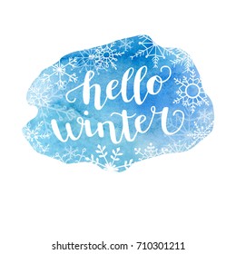 Hello winter. Vector illustration with hand lettering. Hand written quote on bright blue watercolor stain with cute doodle snowflakes. Vibrant texture on white background.