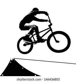 High contrast silhouette of an extreme sports bike rider doing a transfer on a ramp at the skate park.