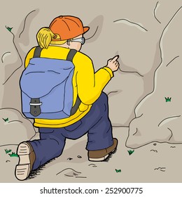 Hiker in yellow kneeling and pointing at rock