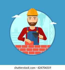 A hipster bricklayer in uniform and hard hat. Bricklayer working with a spatula and a brick in hands on construction site. Vector flat design illustration in the circle isolated on background.