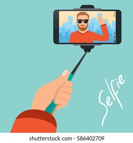 Hipster makes selfie on the background of the city with the help of selfie-stick