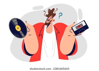 Hipster man holds vinyl record and tape player cassette trying to make choice between analog media. Using vinyl discs and films to reproduce music by retro composers in good quality