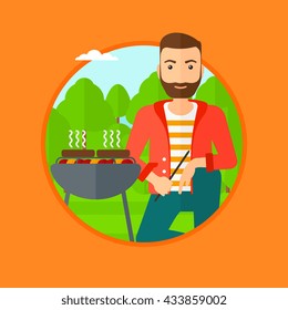 A hipster man sitting next to barbecue grill in the park. Man cooking meat on the barbecue grill. Man having a barbecue party. Vector flat design illustration in the circle isolated on background.