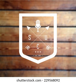 Hipster vector logo shield with crossed arrows and retro mic at blurred wooden background