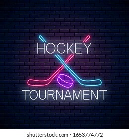 Hockey tournament neon sign with hockey sticks and puck on dark brick wall background. Ice hockey competition logo, emblem, symbol design. Vector illustration.