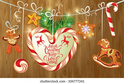 Holiday greeting Card with xmas gingerbread, candy and fir-tree branches. Hand written calligraphic text Merry Christmas and Happy New Year on wooden background. 