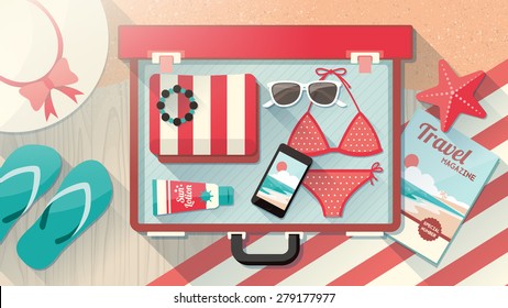 Urlaub am Strand Konzept, Mode weibliche Accessoires in einem offenen Koffer, Bikini, Sonnenbrille, Hut und Handy in einem offenen Vintage Koffer auf Holzboden und Sand