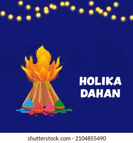 Holika Dahan Celebration Concept With Bonfire, Sugarcane, Bowls Full Of Dry Color (Gulal) And Lighting Garland On Blue Silhouette Buildings Background.