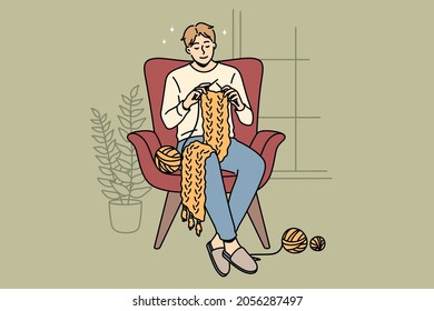 Home hobbies and knitting concept. Young smiling man cartoon character sitting at home in armchair knitting scarf vector illustration 