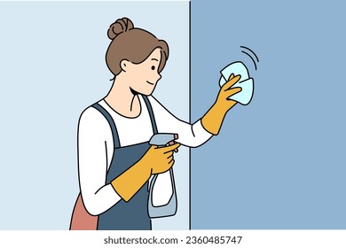 Housewife woman cleaning apartment, wiping wall or glass using antibacterial spray, dressed in apron and gloves. Happy girl works as maid in motel and cleaning preparing room for arrival of guests