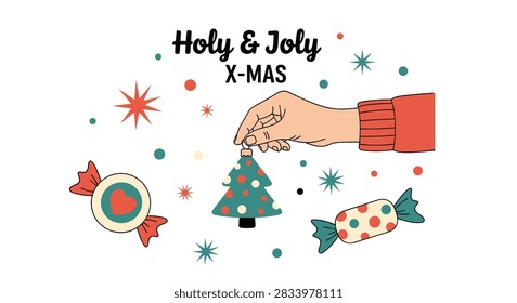Human hand hangs a small Christmas tree ornament amongst a variety of festive stars, candies, and holiday text.