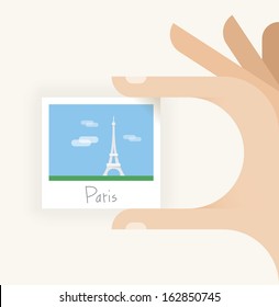 Human hand holding Paris photo with Eiffel Tower.