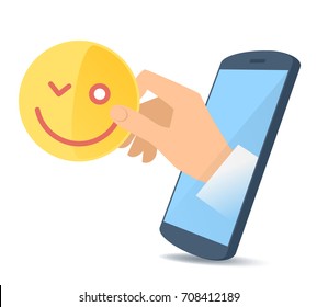 A human hand from the mobile phone's screen holds a yellow emoji face. Modern technology, smart phone apps, emoticon and emotion flat concept illustration. Vector design element isolated on white.