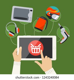 Human hands hold and tap on screen of smart tablet with buy button with shopping basket, goods are displayed around tablet. Buying online with mobile gadget as online shopping concept