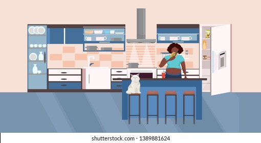 hungry african american woman eating burger near open refrigerator unhealthy lifestyle concept overweight girl eat fast food modern kitchen interior portrait horizontal
