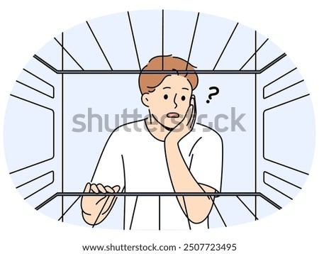 Hungry man sees empty refrigerator and is nervous about lack food due to poverty and financial crisis. Young embarrassed guy looks into refrigerator compartment surprised by lack products on shelves