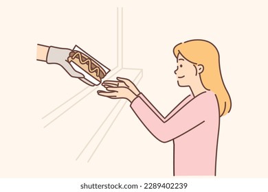 Hungry woman buys hot dog in fast food restaurant or street catering store with delicious calorie sandwiches. Happy girl wants to try hot dog from food truck or cafe to satisfy hunger 